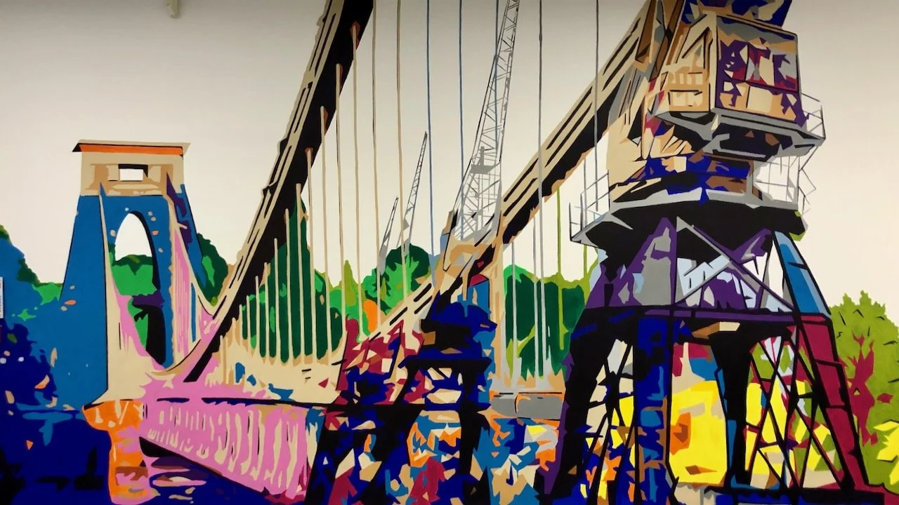 Digital artwork of a suspension bridge with colorful geometric shapes and a city skyline in the background.