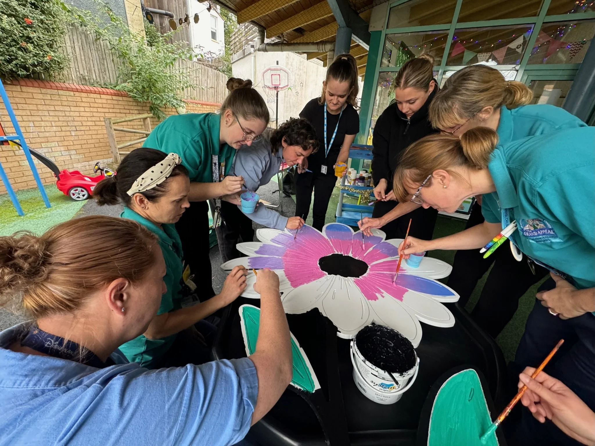 Group of women painting a large flower-shaped object outdoors.