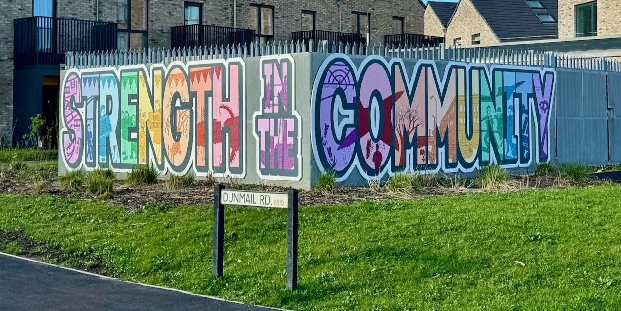 Colorful mural on a city wall with the words "Strength in the Community" in large, decorated letters.
