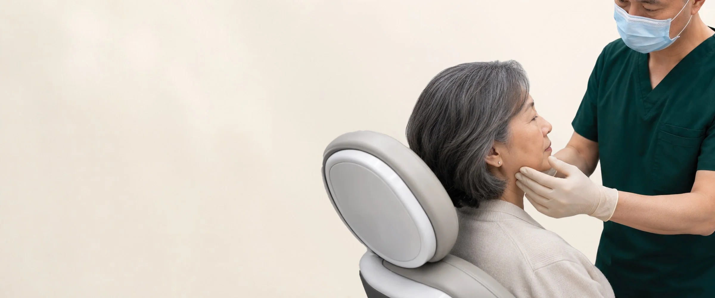 A healthcare professional wearing a face mask and gloves examines a woman with gray hair in a dental or medical chair.