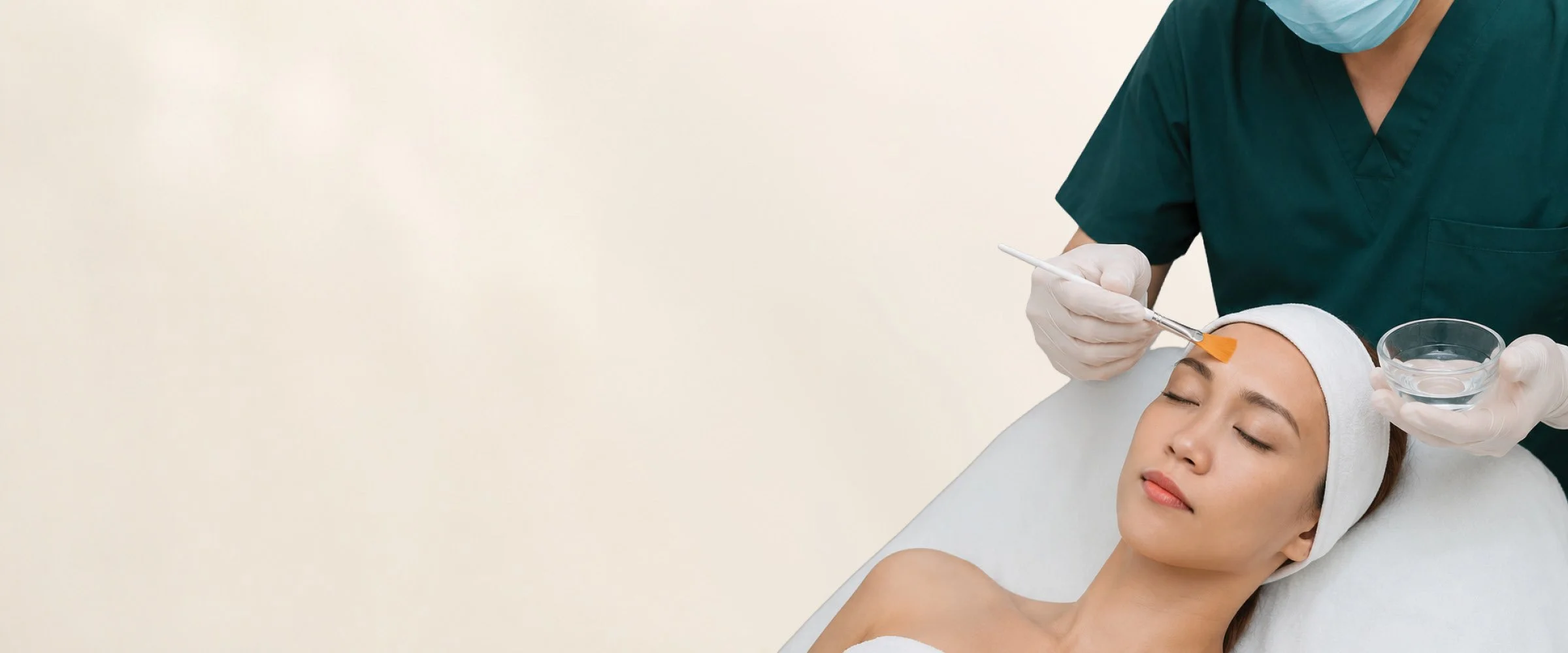 A woman receiving a facial treatment from a skincare professional in a clinical setting.