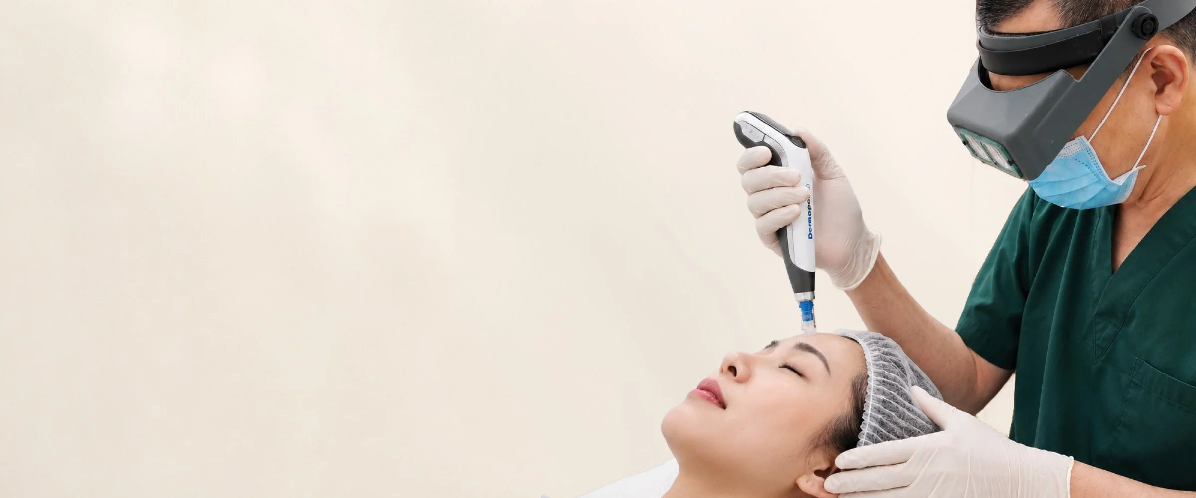 Medical professional in scrubs, wearing magnifying glasses, a face mask, and gloves, uses a device on a woman's face in a clinical setting.