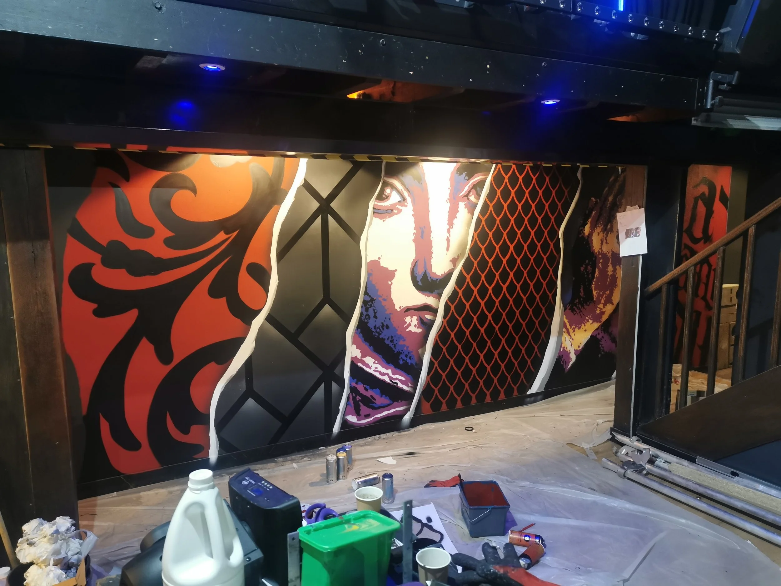Une œuvre d'art de style pop art représentant un visage féminin, avec des couleurs vives et des motifs graphiques, se trouve sur une surface verticale dans un espace intérieur.