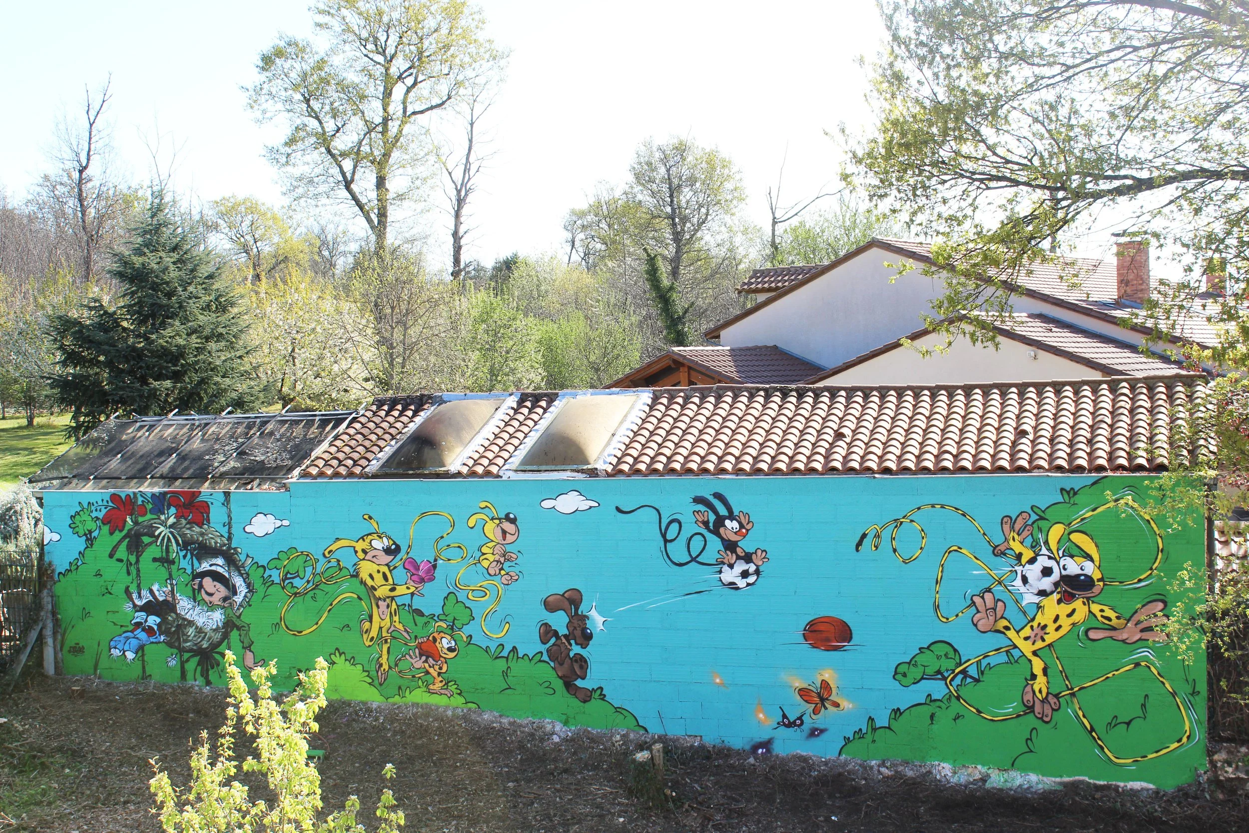 Un mur peint avec une fresque colorée représentant des personnages de dessins animés, tels que Mickey Mouse et d'autres animaux, avec un fond bleu et des éléments verts de végétation autour.