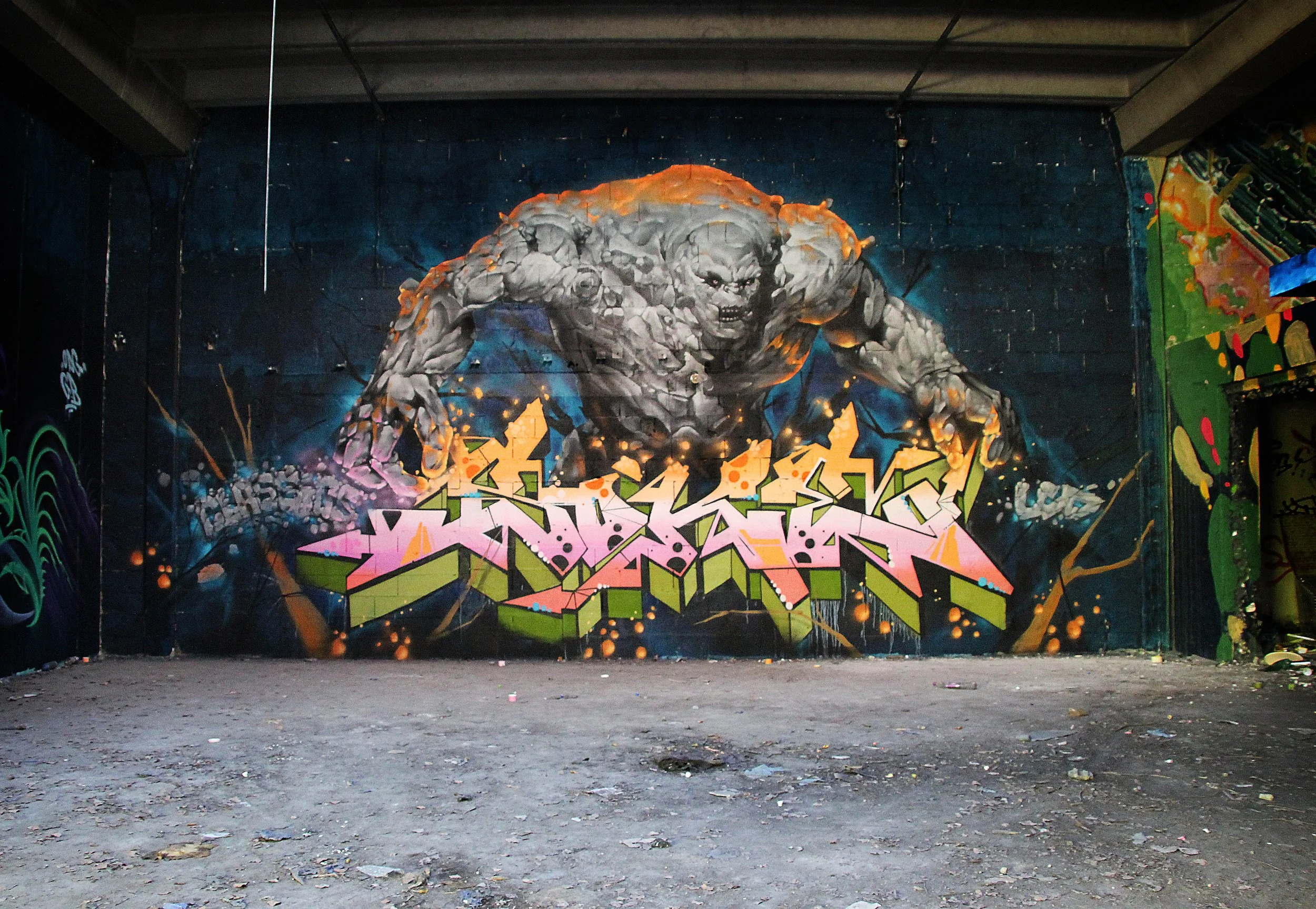 Un graffiti représentant un personnage de pierre semblable à un géant ou un monstre, dans une ambiance urbaine nocturne avec des couleurs vibrantes, des décorations de graffiti sur le mur en arrière-plan et un sol en terre.