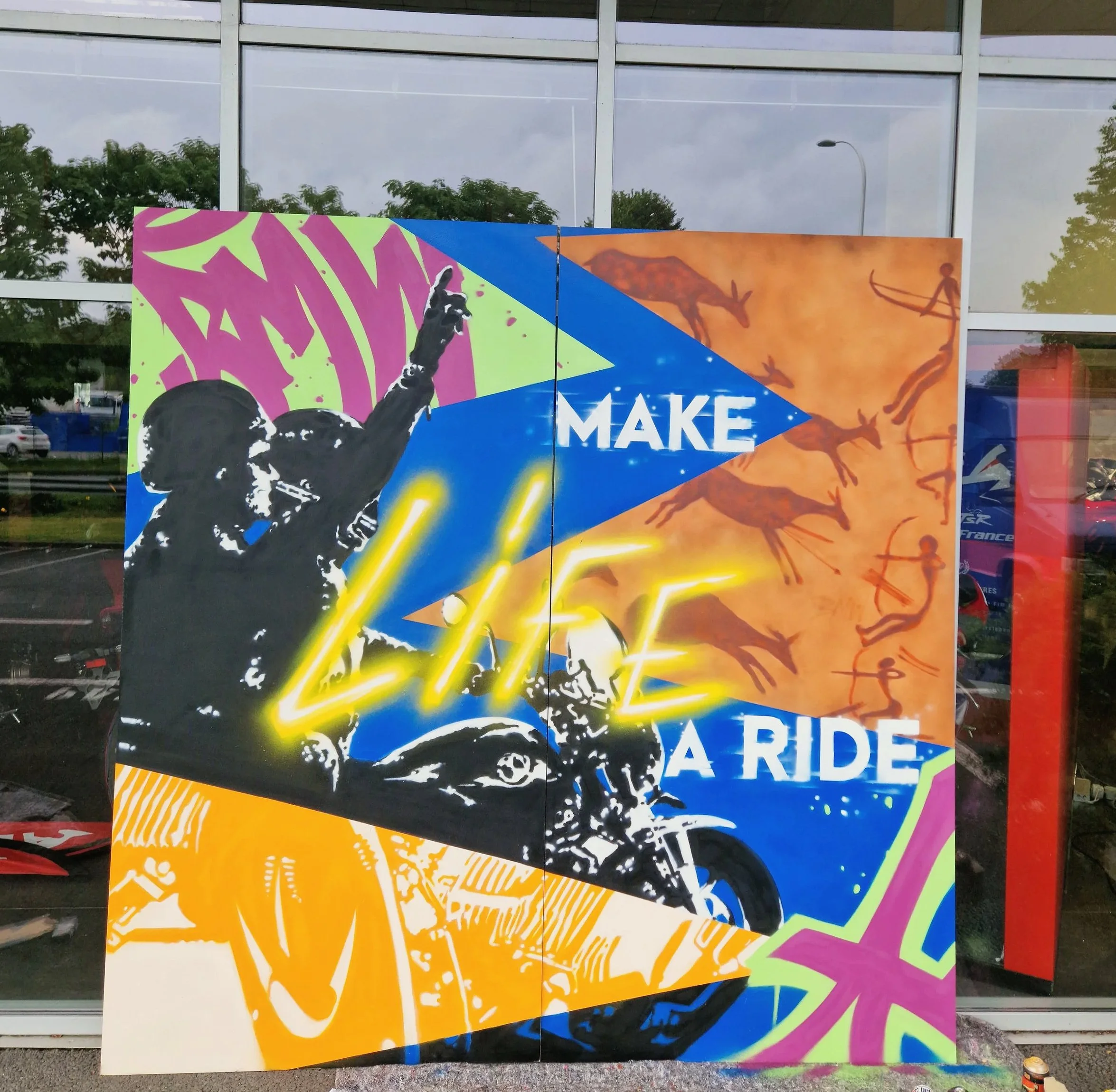Un panneau publicitaire coloré avec un chien qui saute, des montagnes en arrière-plan, et le texte partiellement visible "MAKE A RIDE".