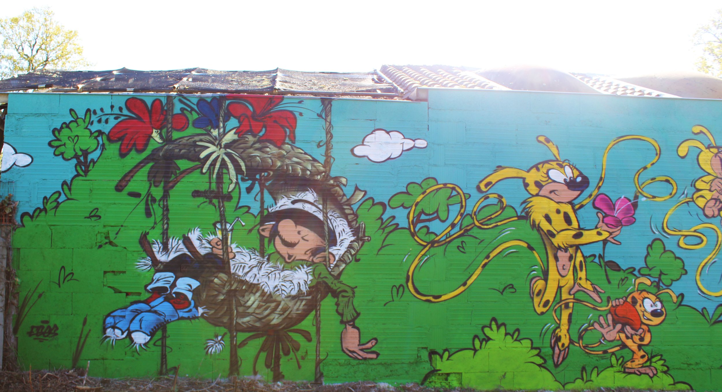 Murale colorée représentant un lionceau, une tigresse, une chouette dans un nid, et un petit singe, avec un fond de ciel bleu et de végétation verte.
