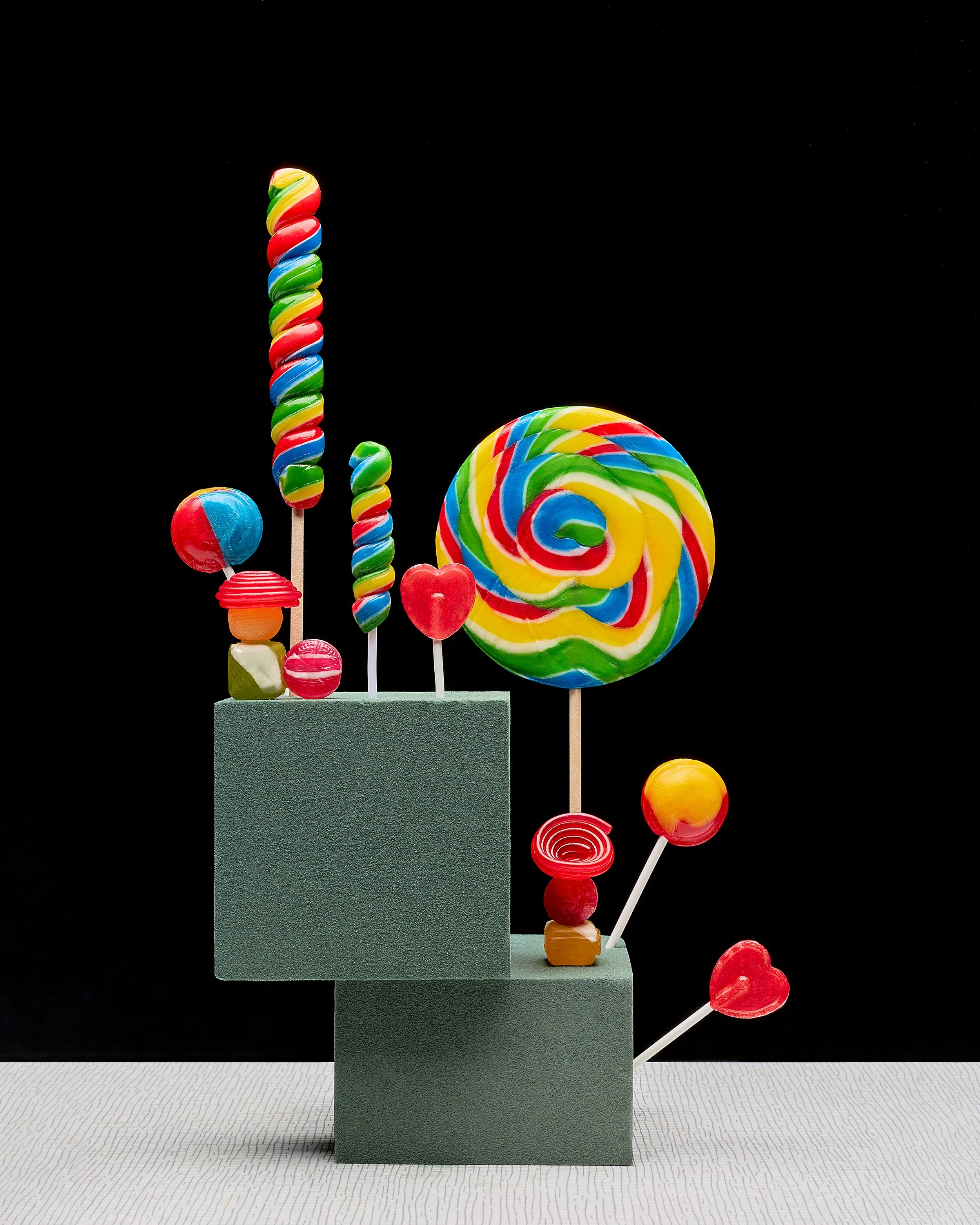 Colorful candy lollipops and sweets arranged on a gray platform with a black background.