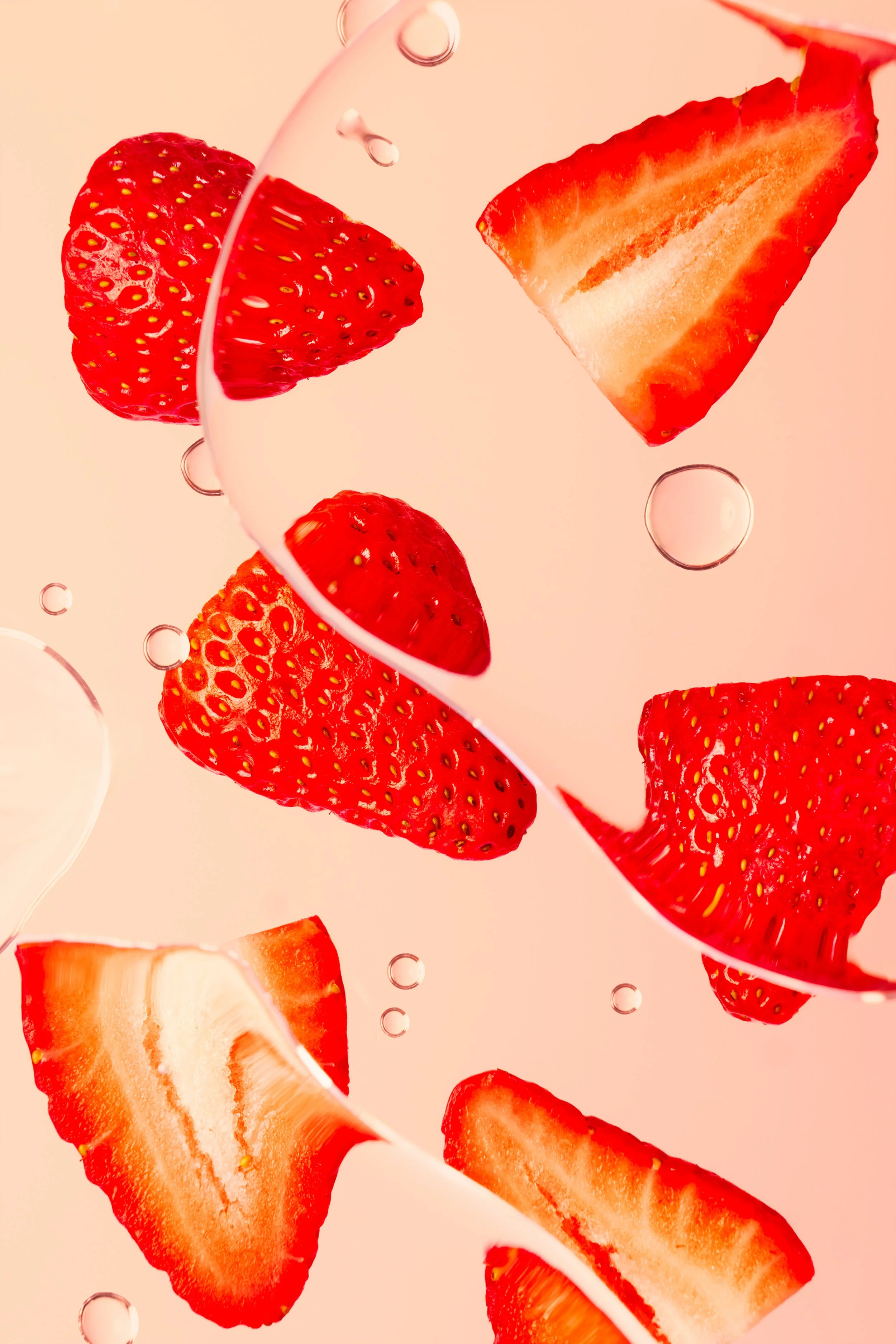 Slices of strawberries and a piece of watermelon floating against a pink background with water bubbles.