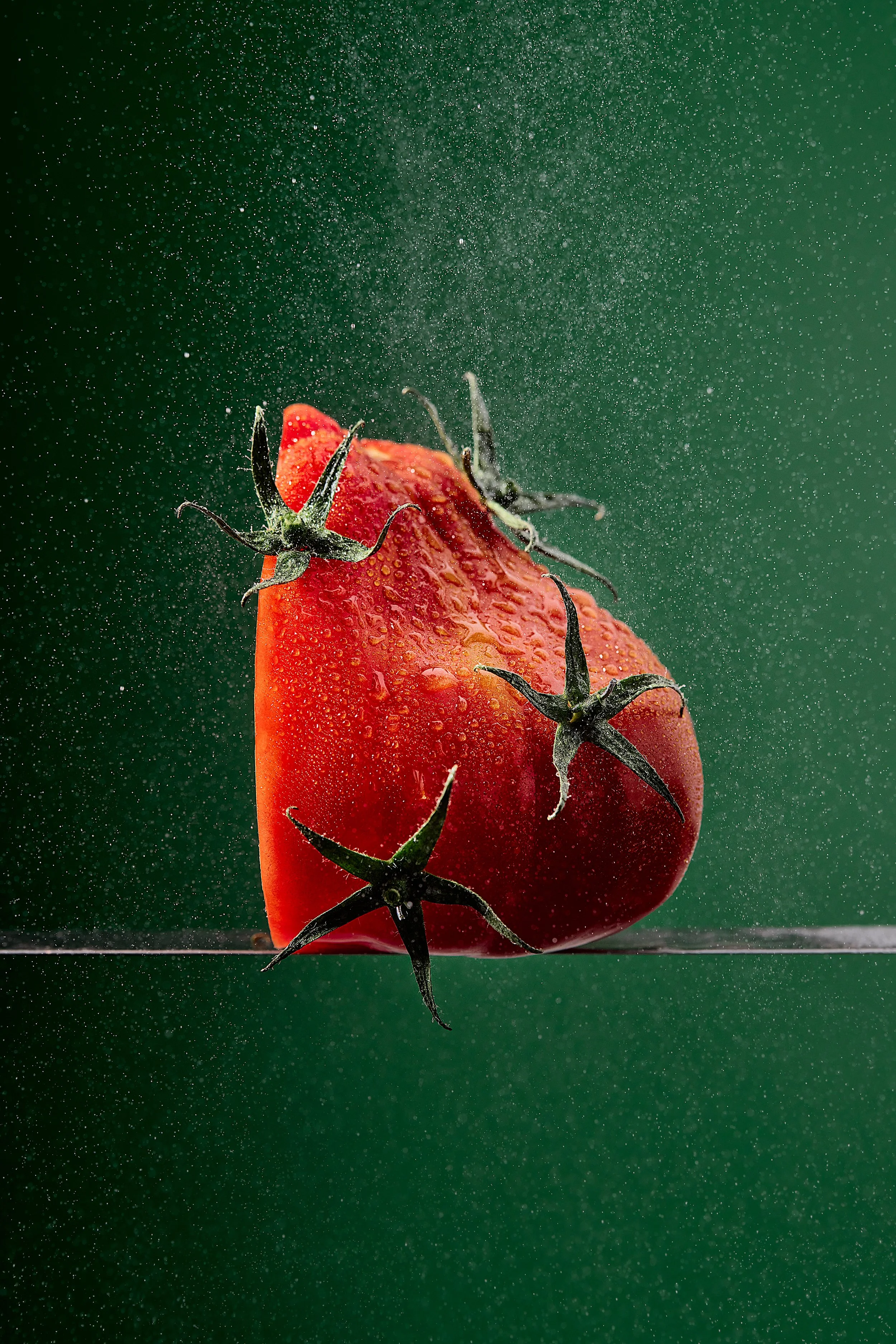 Close-up of a red tomato with water droplets, balancing on a knife with water mist spray around it