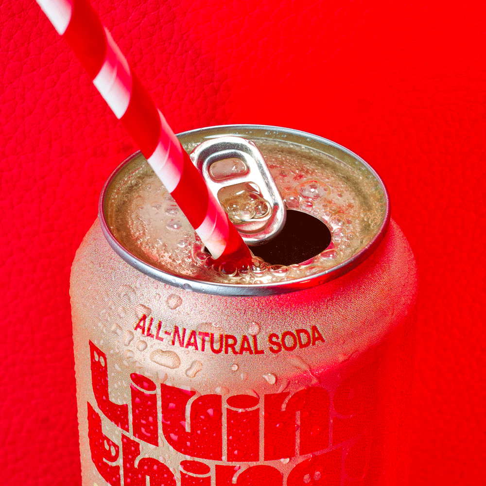 Can of Living Things all-natural soda with a red and white striped straw on a red surface.