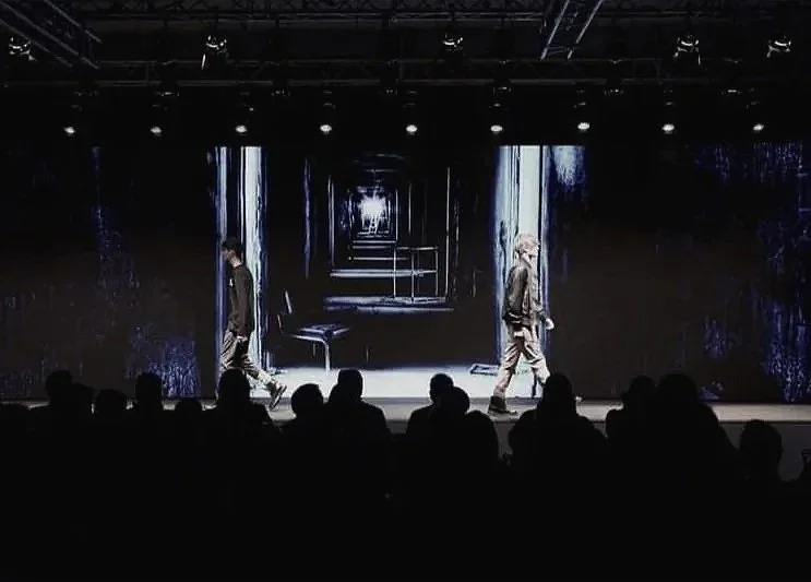 Scena con due persone che camminano su un palco con schermo digitale che mostra un tunnel illusorio.