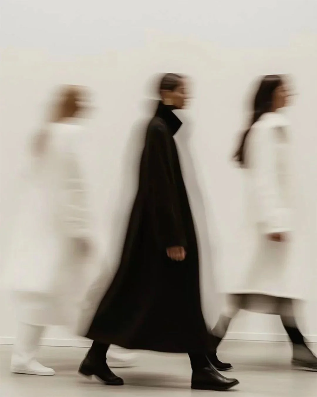 Tre donne camminano in fila, una vestita di nero, le altre due di bianco, sfocate in movimento.