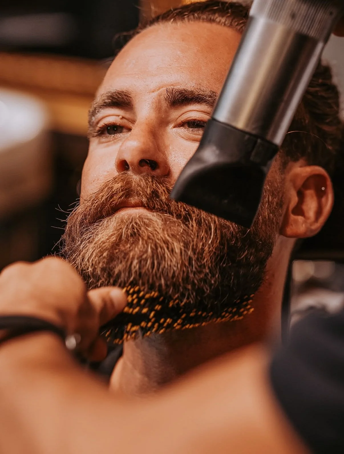 Man with a neatly trimmed beard and mustache getting a close shave from a barber using a straight razor.