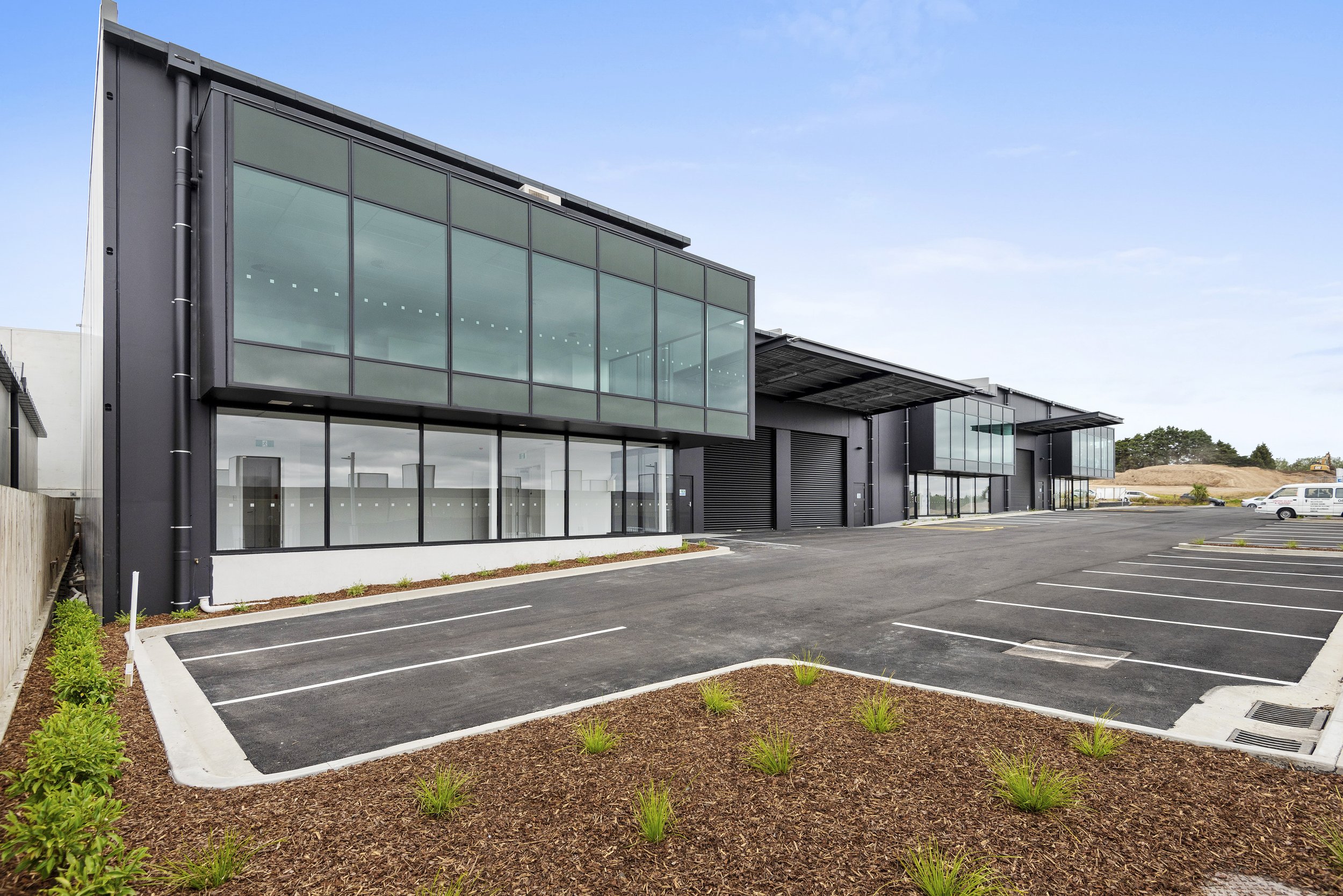 Modern commercial building with large glass windows, black exterior, and an empty parking lot in front, under a clear blue sky.