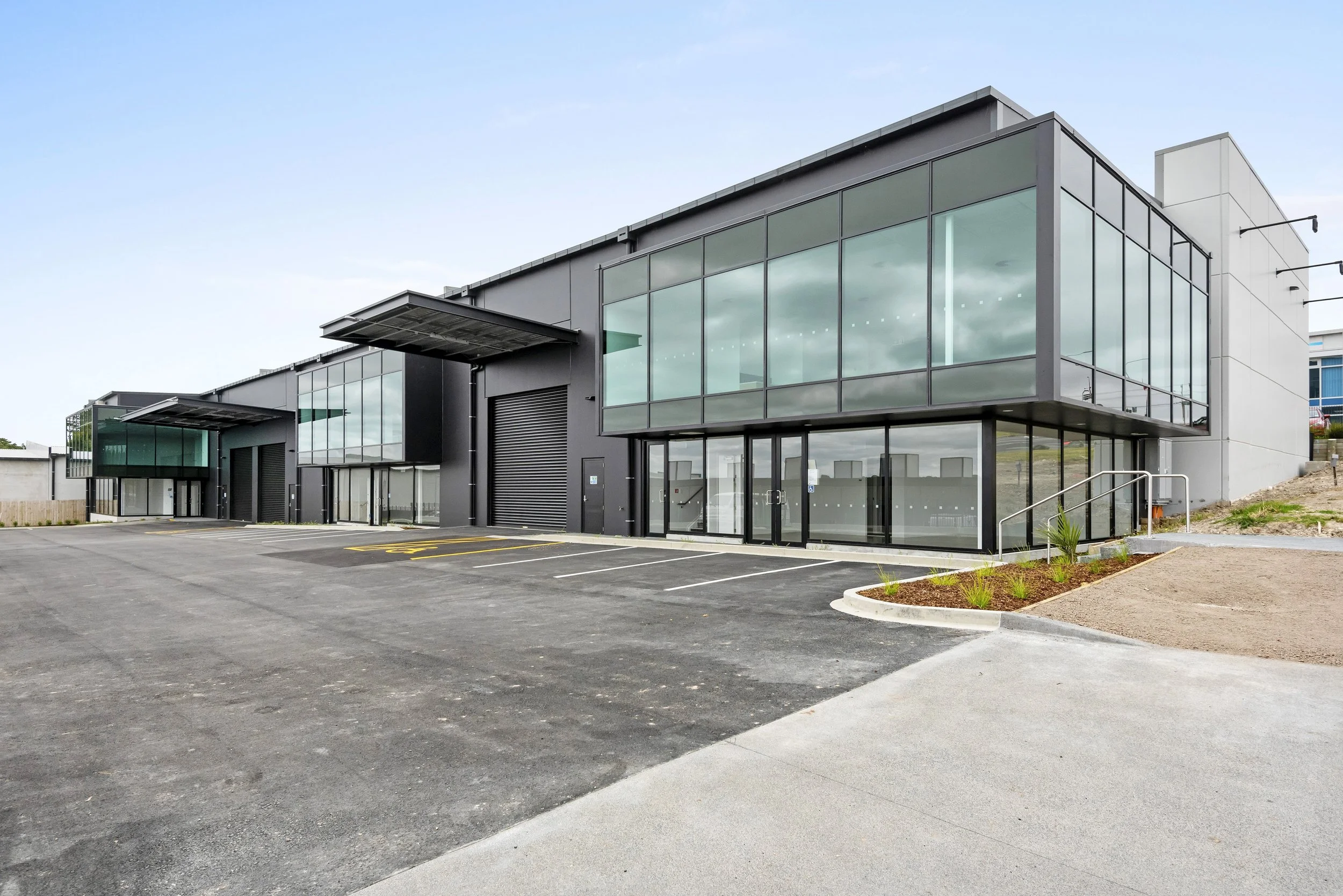 Modern commercial building with large glass windows, a parking lot, and landscaped areas.