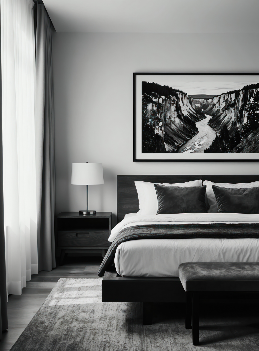 Modern bedroom with black and white decor, featuring a bed with black pillows, a nightstand with a white lamp, and framed landscape artwork above the headboard. Light from a large window with curtains illuminates the room.
