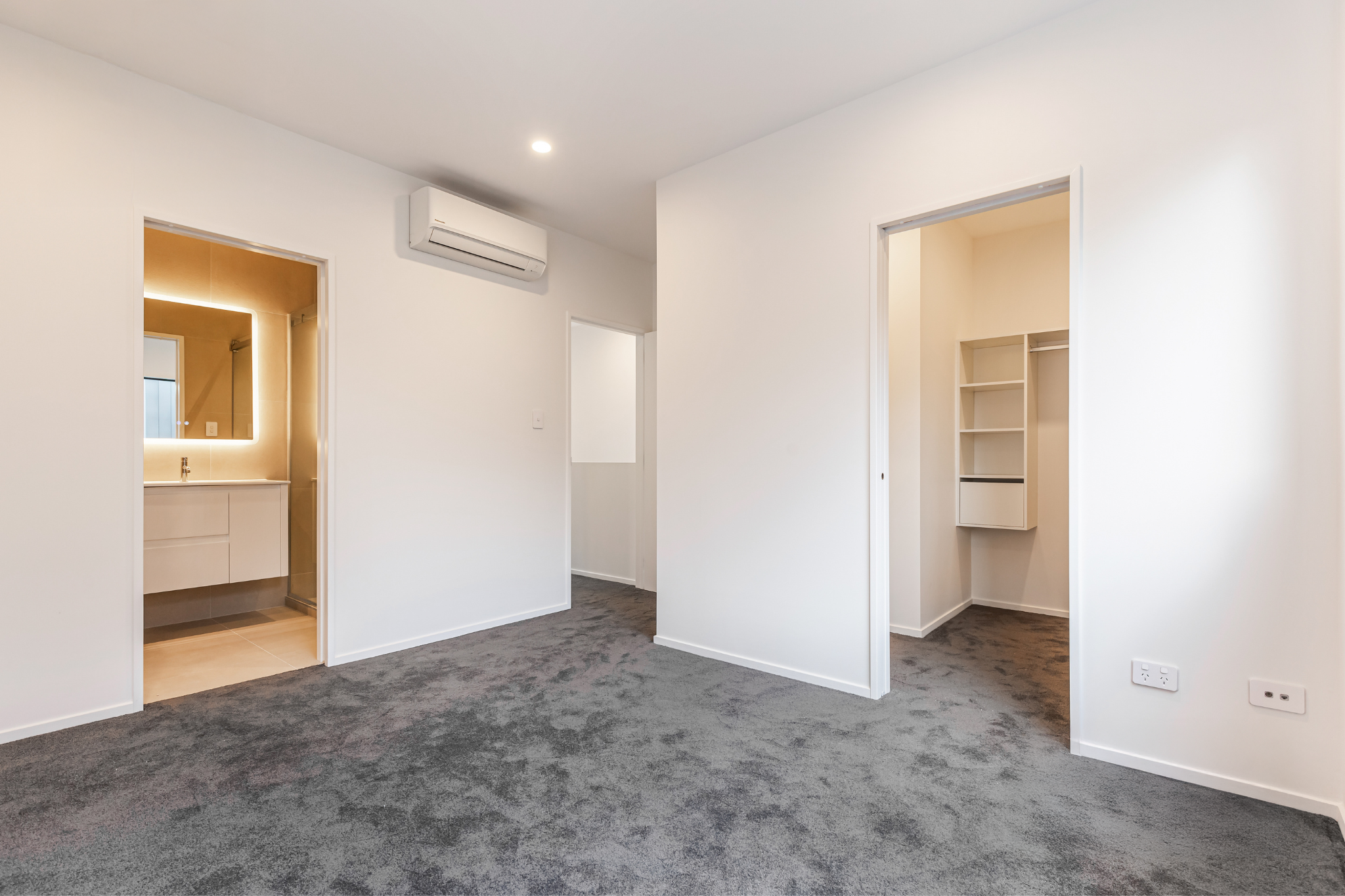 Empty modern living room with white walls, grey carpet, and open closet spaces.