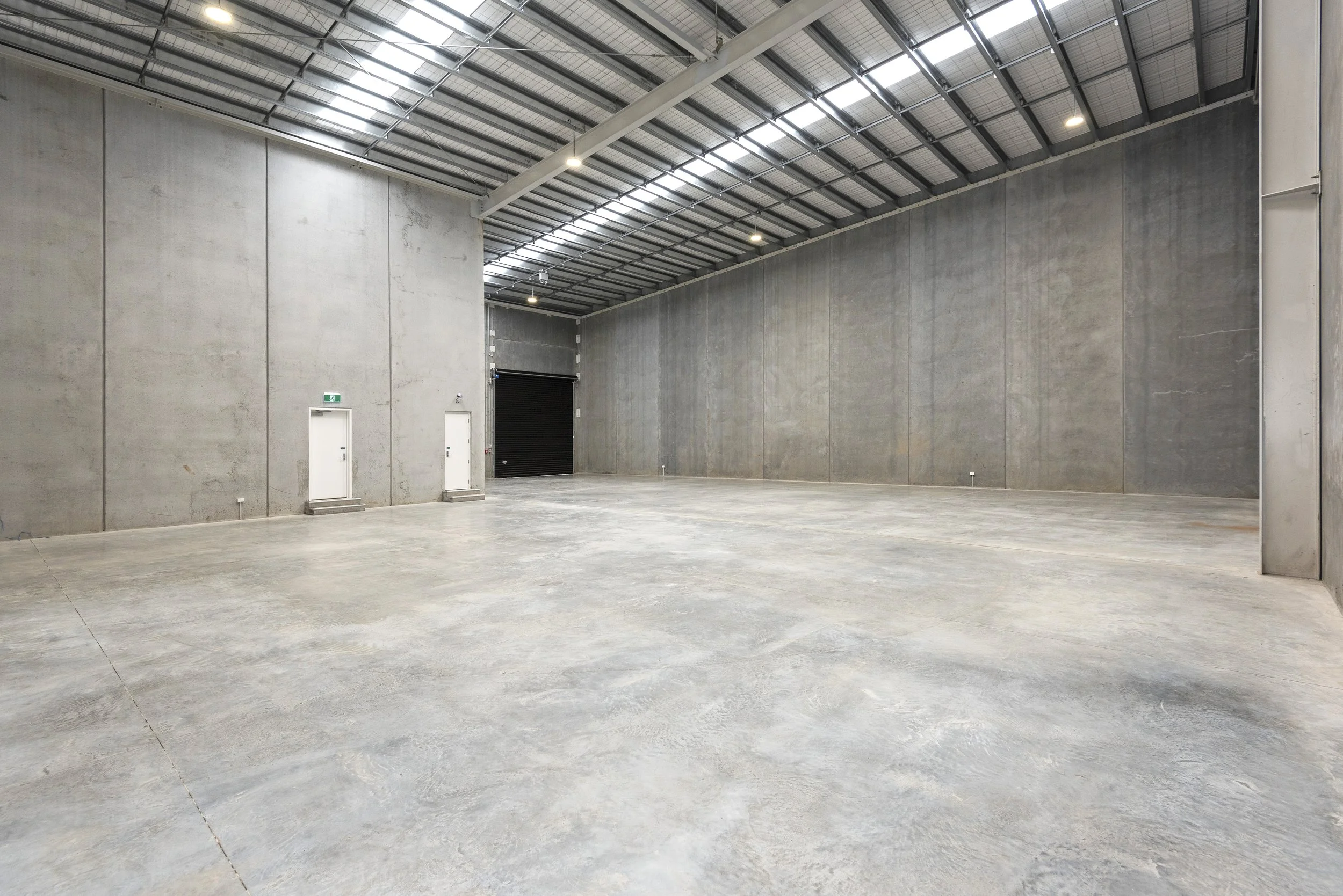 Empty industrial warehouse with high ceiling, concrete walls, and large roller door.