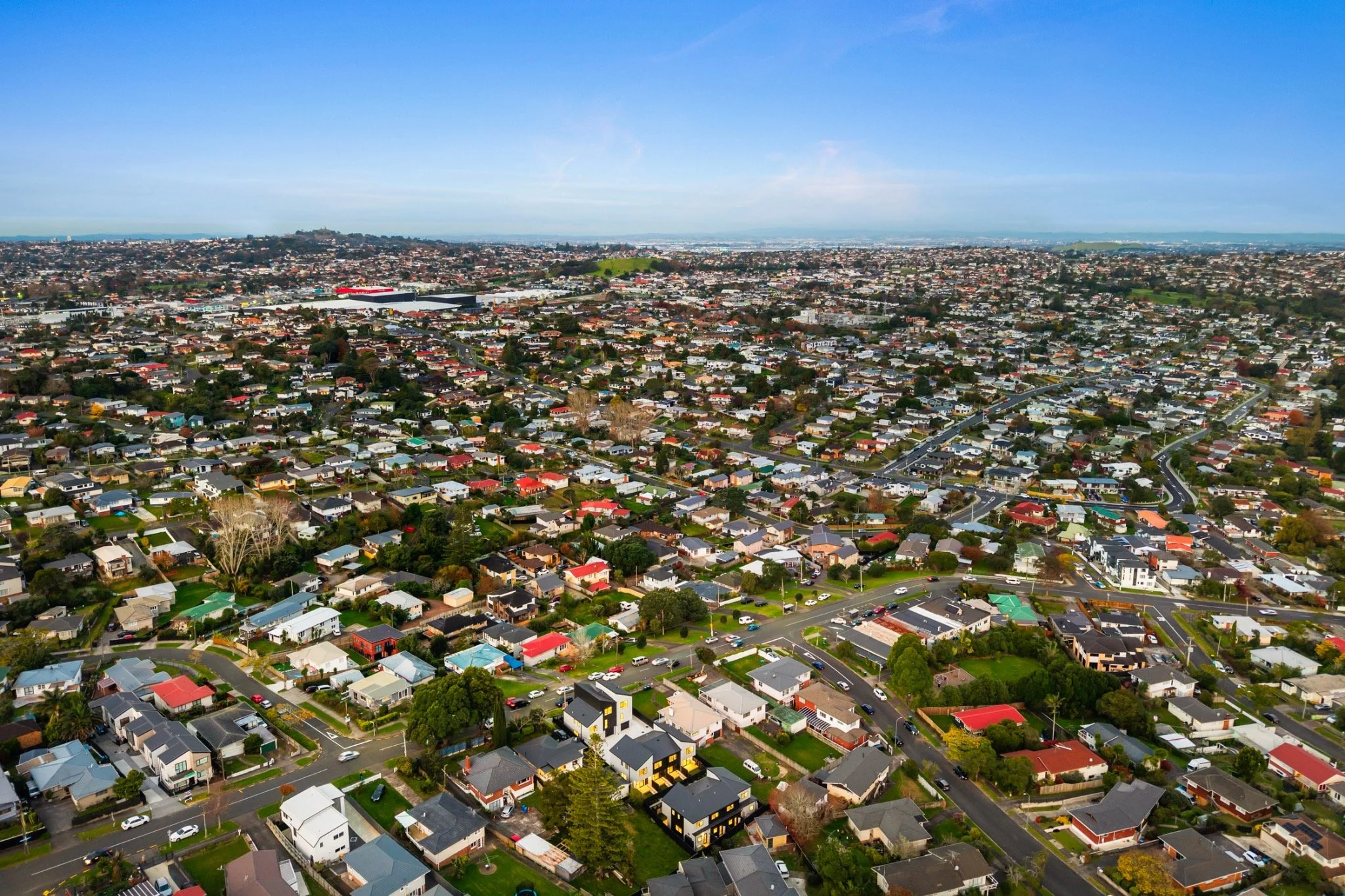 Aerial view of a densely populated residential neighborhood with houses, streets, and some commercial buildings, under a blue sky.