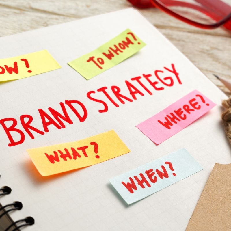 A white sheet of paper with highlighter notes about brand strategy, labeled with questions: "Who?", "To Whom?", "What?", "Where?", and "When?" in bold colored handwriting.
