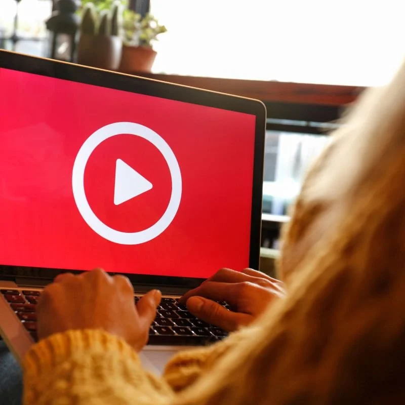 Person using a laptop with a red screen and a white play button on it.