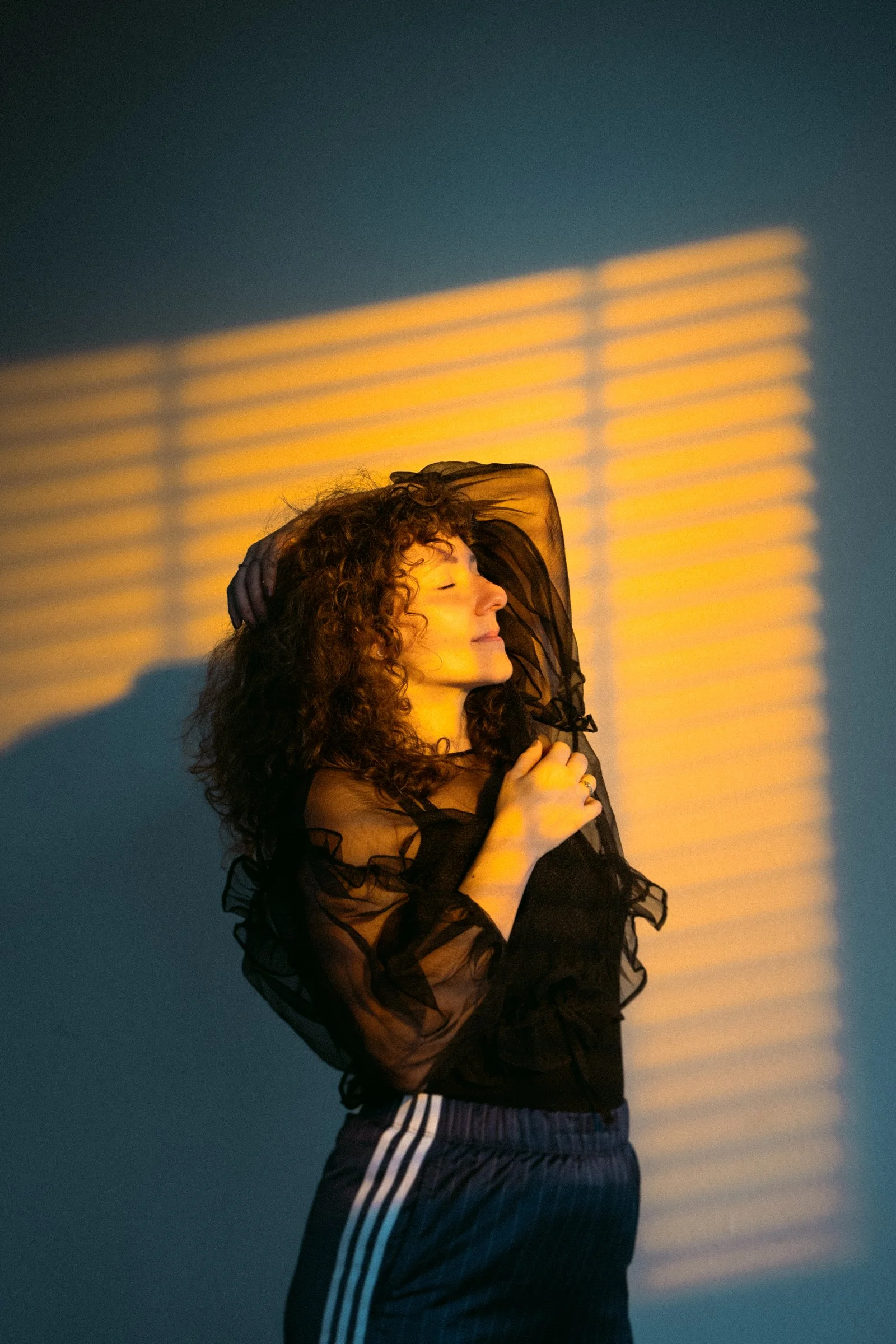 Coco von high on prana, die im Sonnenuntergang in die Kamera lächelt, trägt einen schwarzen transparenten Pullover mit Rüschen und Sporthosen mit Streifen.