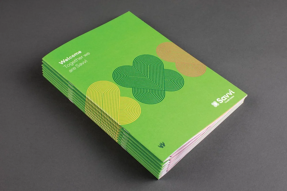 A stack of printed green booklets, the cover motif drawn as three overlapping hearts in concentric lines