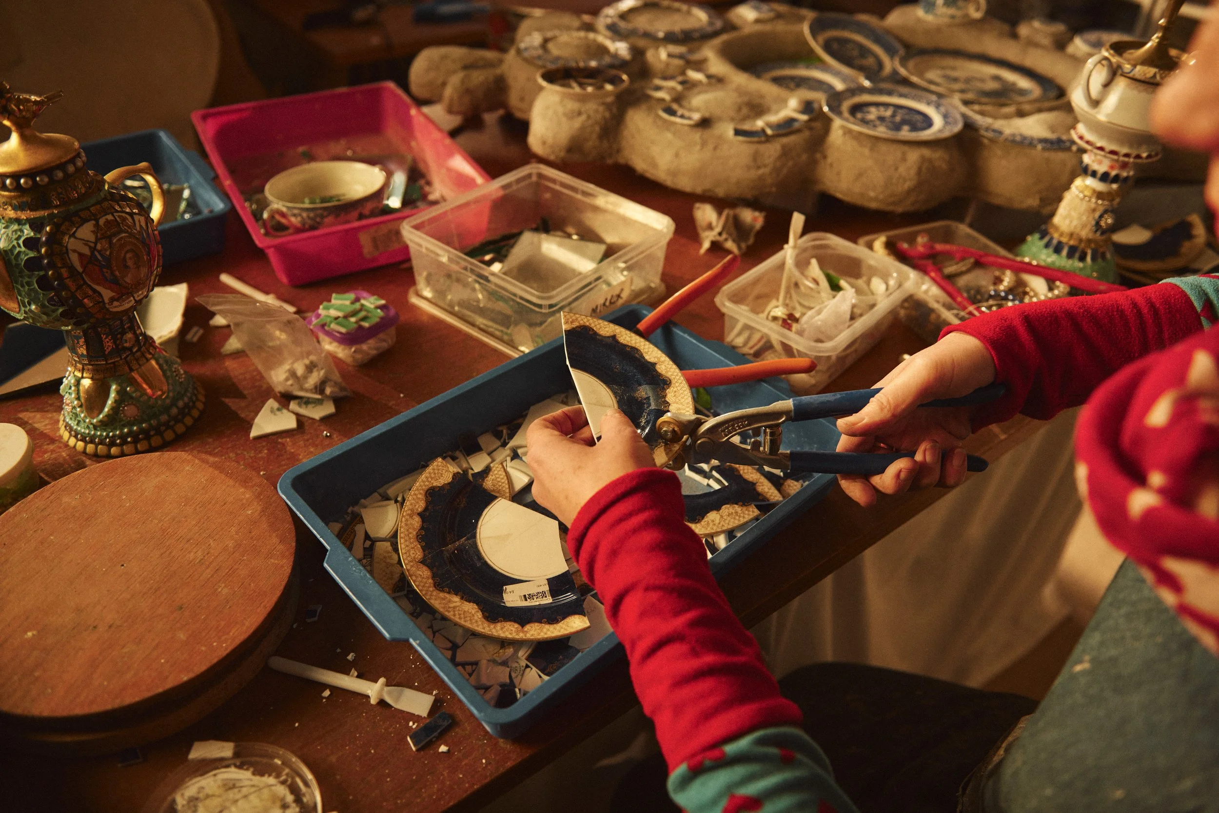 Anne trimming decorative ceramic plates and pieces on a table. 