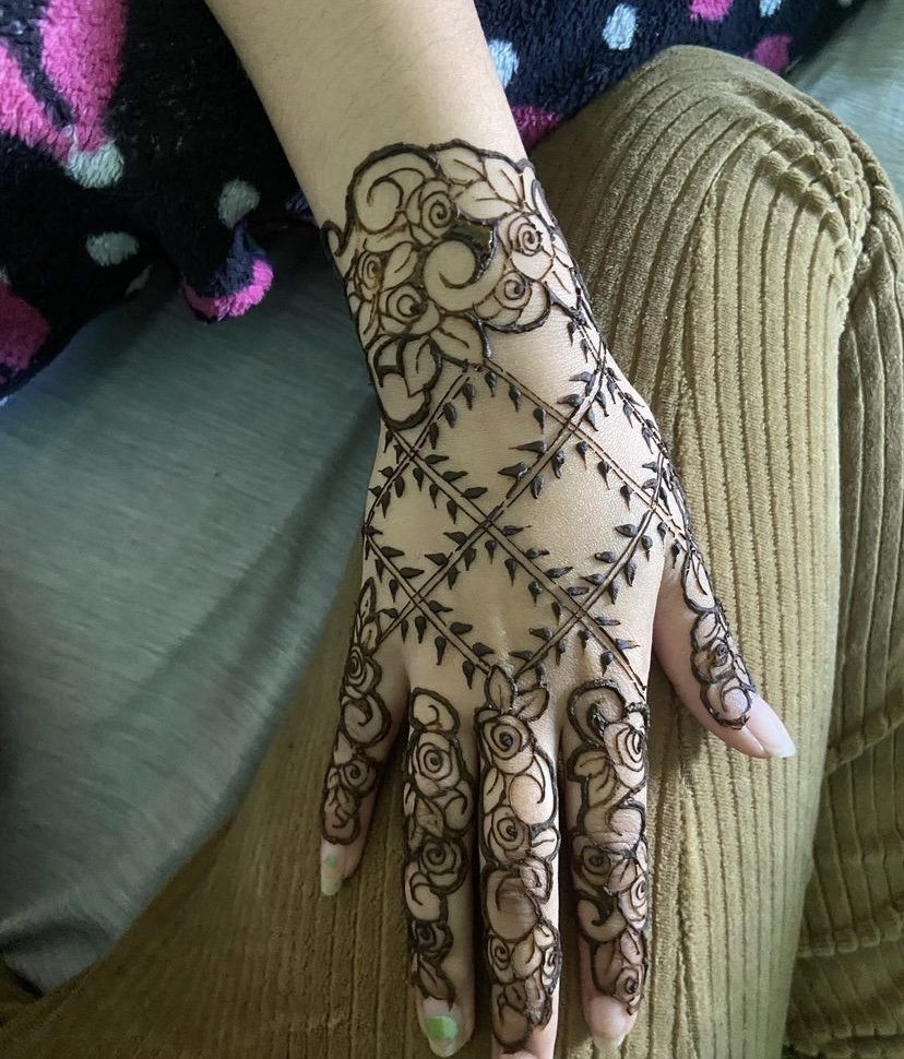 A hand with intricate henna tattoo designs, including roses, spirals, and leaf patterns.