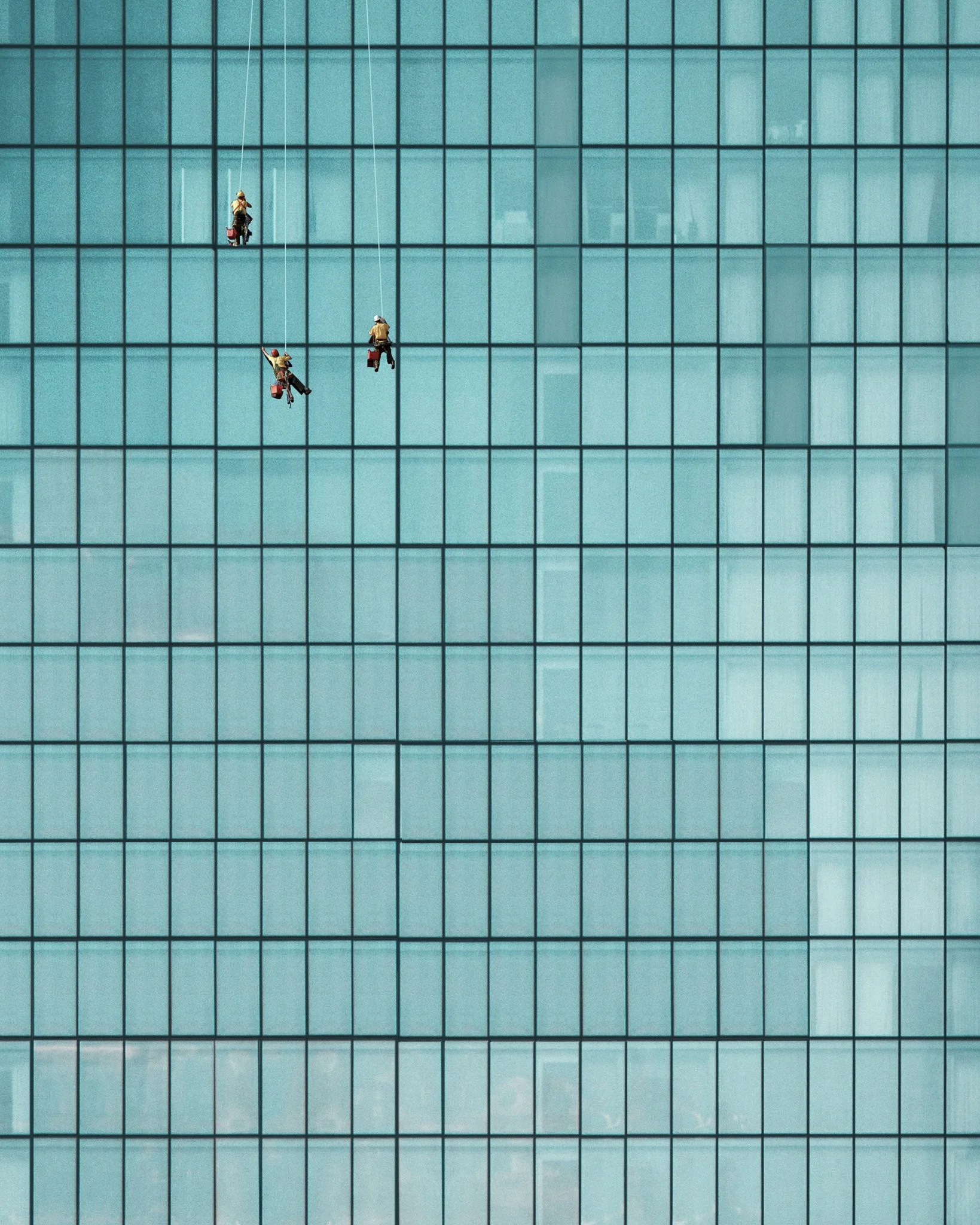 Four miniature workers are cleaning the glass windows of a tall building using squeegees, with two workers on the upper level and two on the lower level.