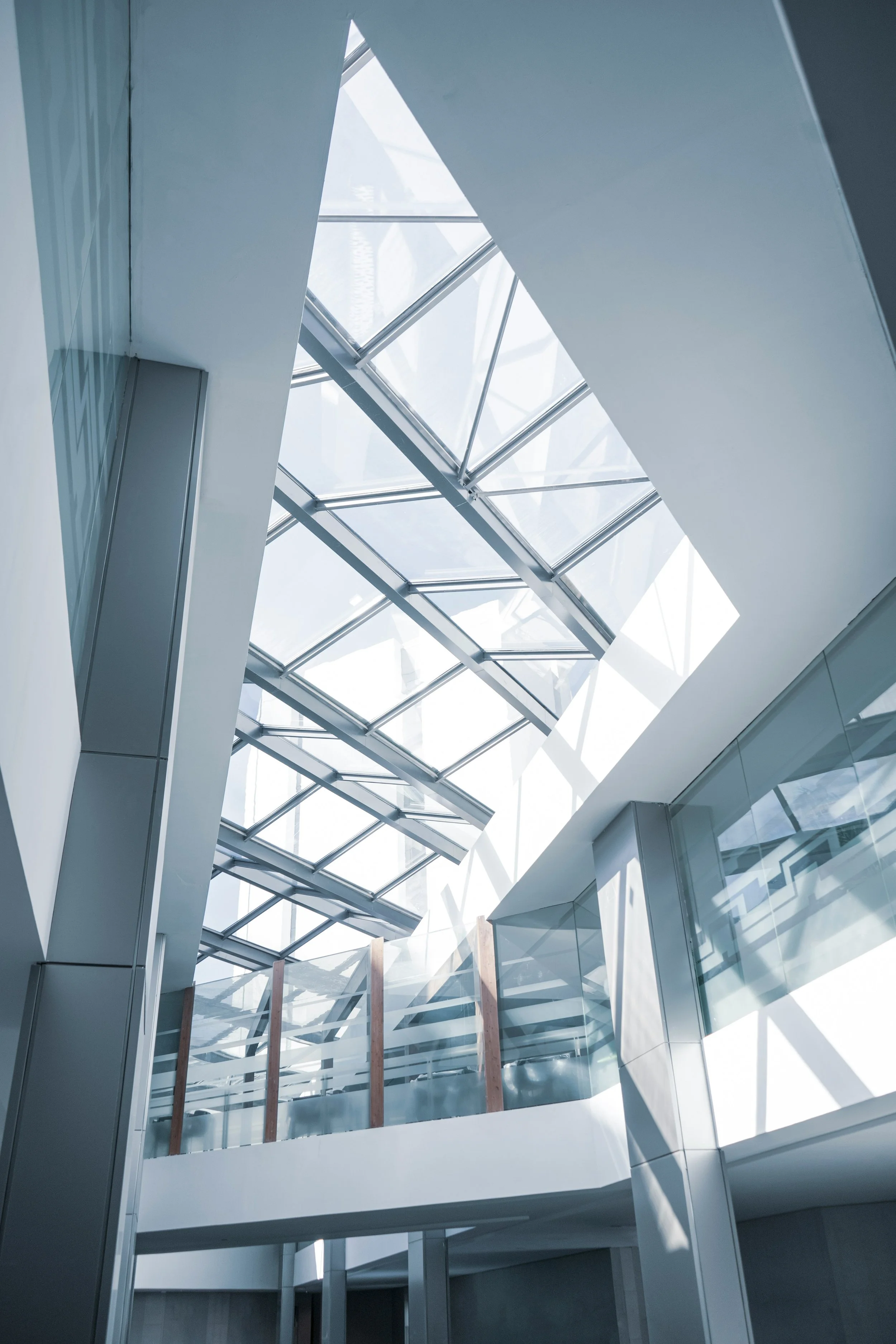 Modern interior with a tilted glass ceiling, white walls, and steel framing, featuring a staircase with glass railings.