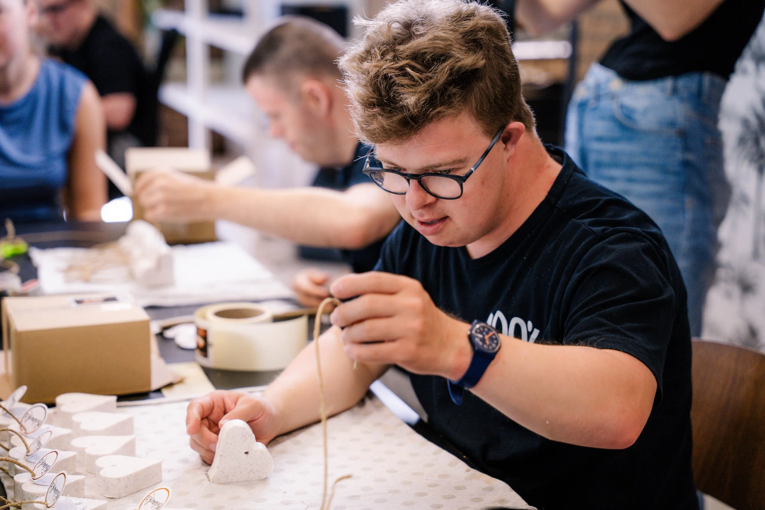 Een jongen met bril en horloge die bezig is met het maken van handgemaakte decoraties op een tafel.