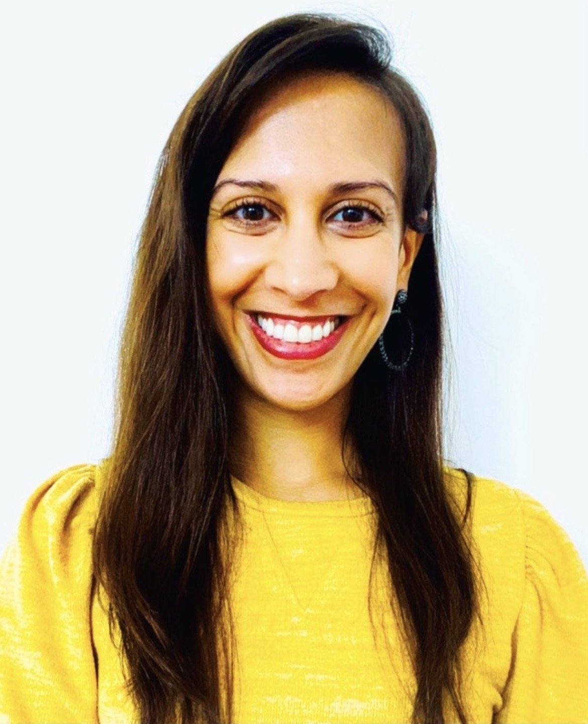 A woman with long brown hair smiling, wearing a bright yellow top, against a plain white background.