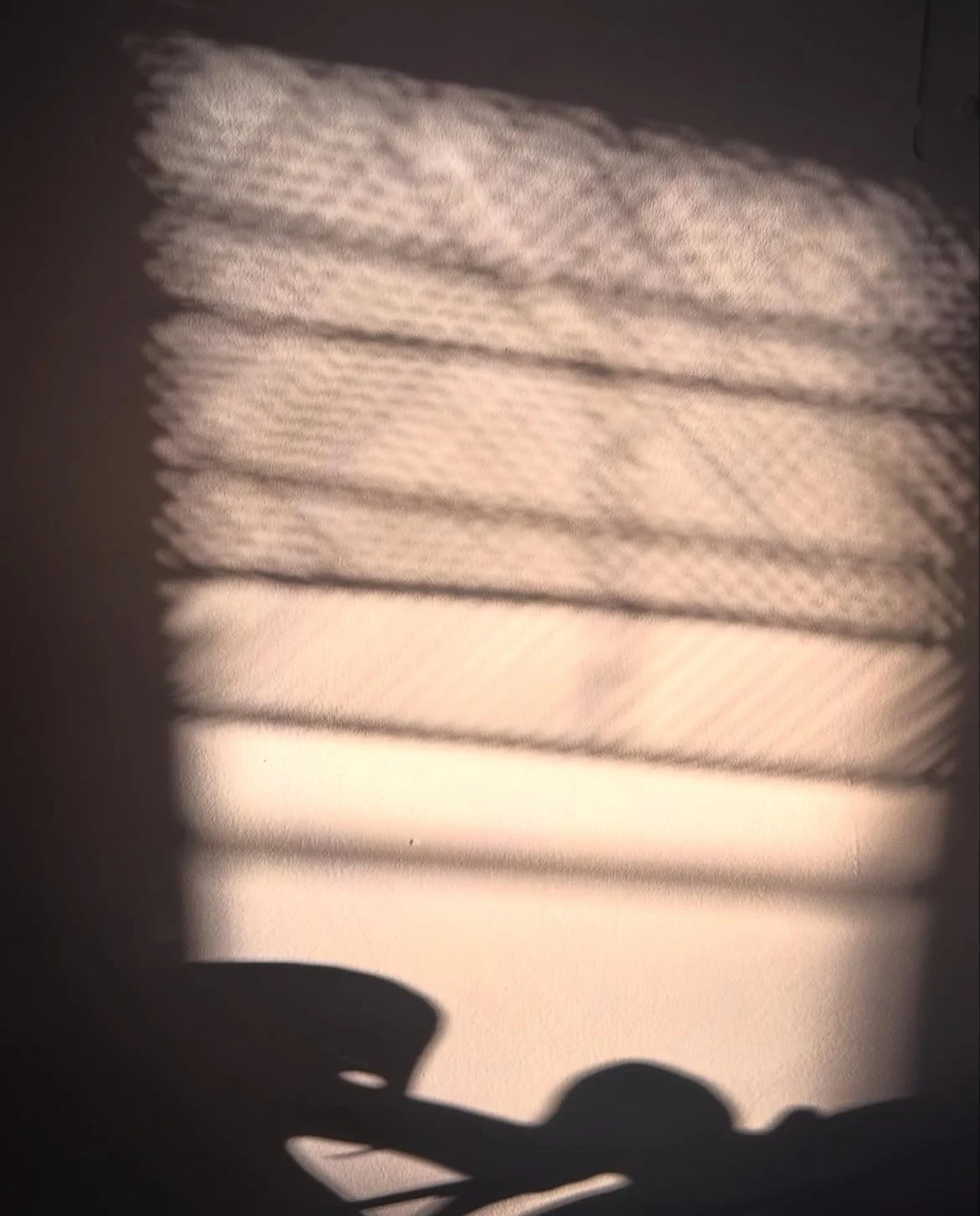 Shadow of a hand with a smiley face on a textured wall created by sunlight shining through window blinds.