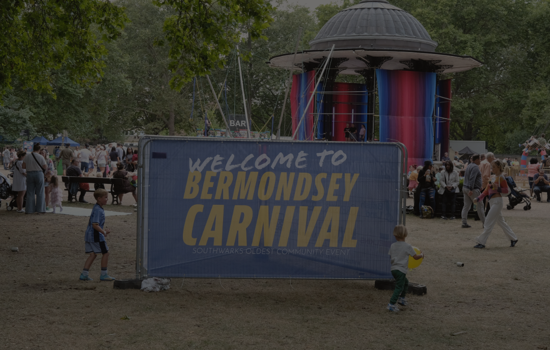 Children playing near a sign that reads "Welcome to Bermondsey Carnival" at a busy outdoor community event with a carousel and trees in the background.