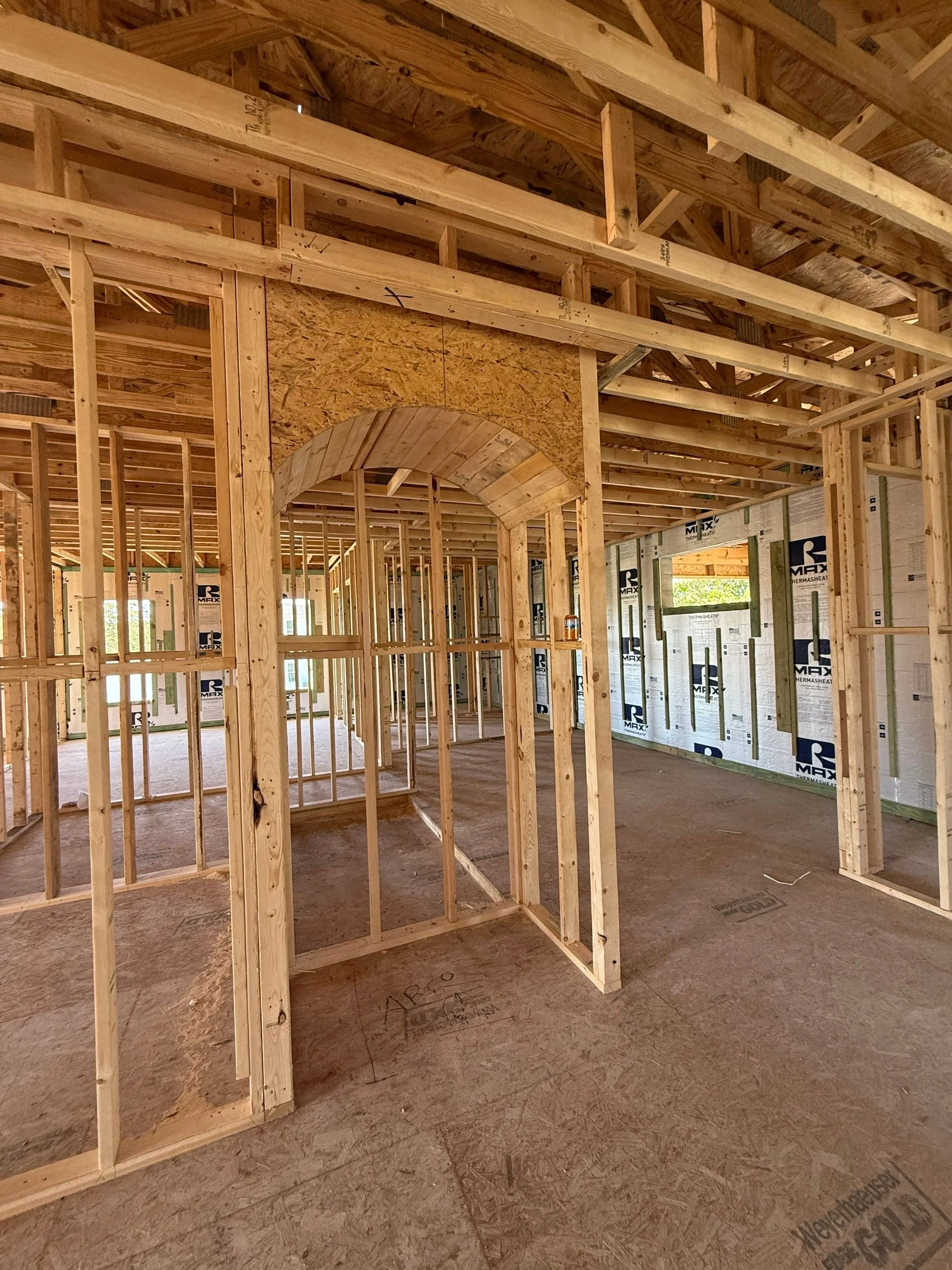 Interior view of a house under construction, showing wooden framing, door openings, and insulation on the walls.