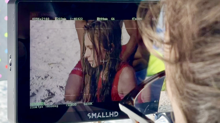 Photo of a camera monitor capturing a woman with wet hair in a red top on a beach.
