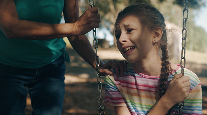 A girl on a swing appearing distressed, with an adult holding the swing's chain quietly nearby.