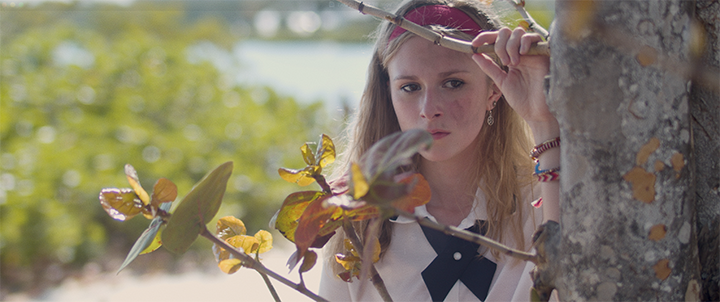 Young woman peering through tree branches outdoors on a sunny day.