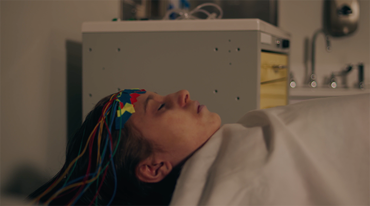 Person lying in a hospital bed with electrodes on their head connected to wires.