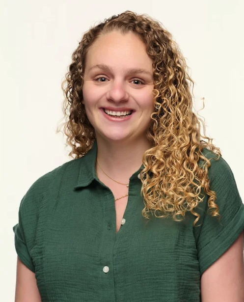 A young woman with curly blonde hair smiling and wearing a green shirt.