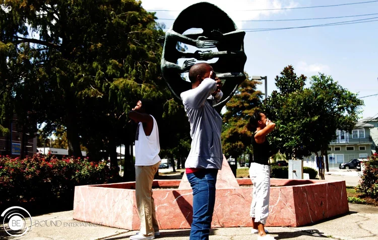Three people standing near the Alabama State Capitol building in Montgomery, Alabama, with their hands on their faces, in front of a large statue of a woman holding a child.