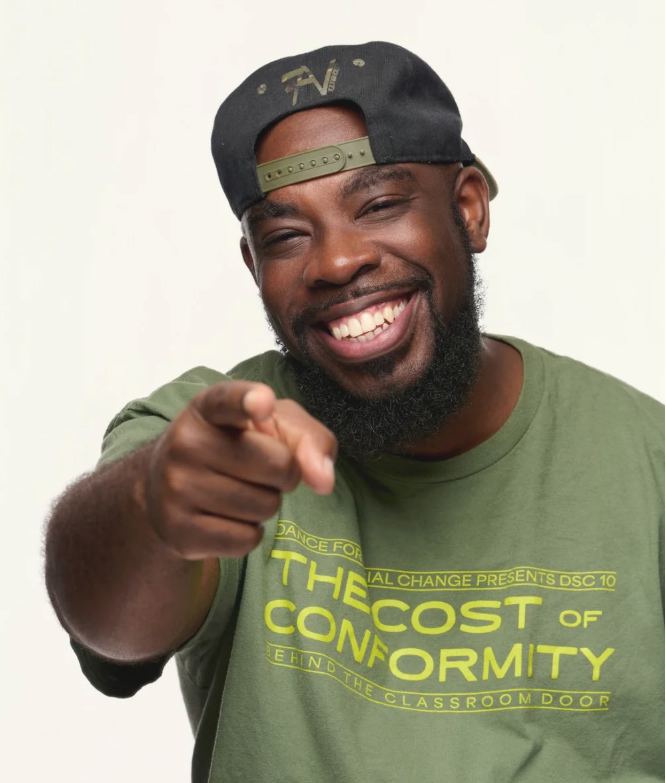 A smiling man wearing a green T-shirt and a black snapback hat, pointing towards the camera.