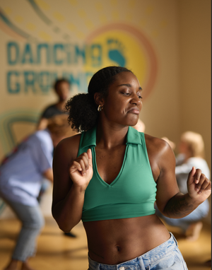 A woman in a green sports bra dancing at a dance fitness class, with other participants and a 'Dancing with Gramps' banner in the background.