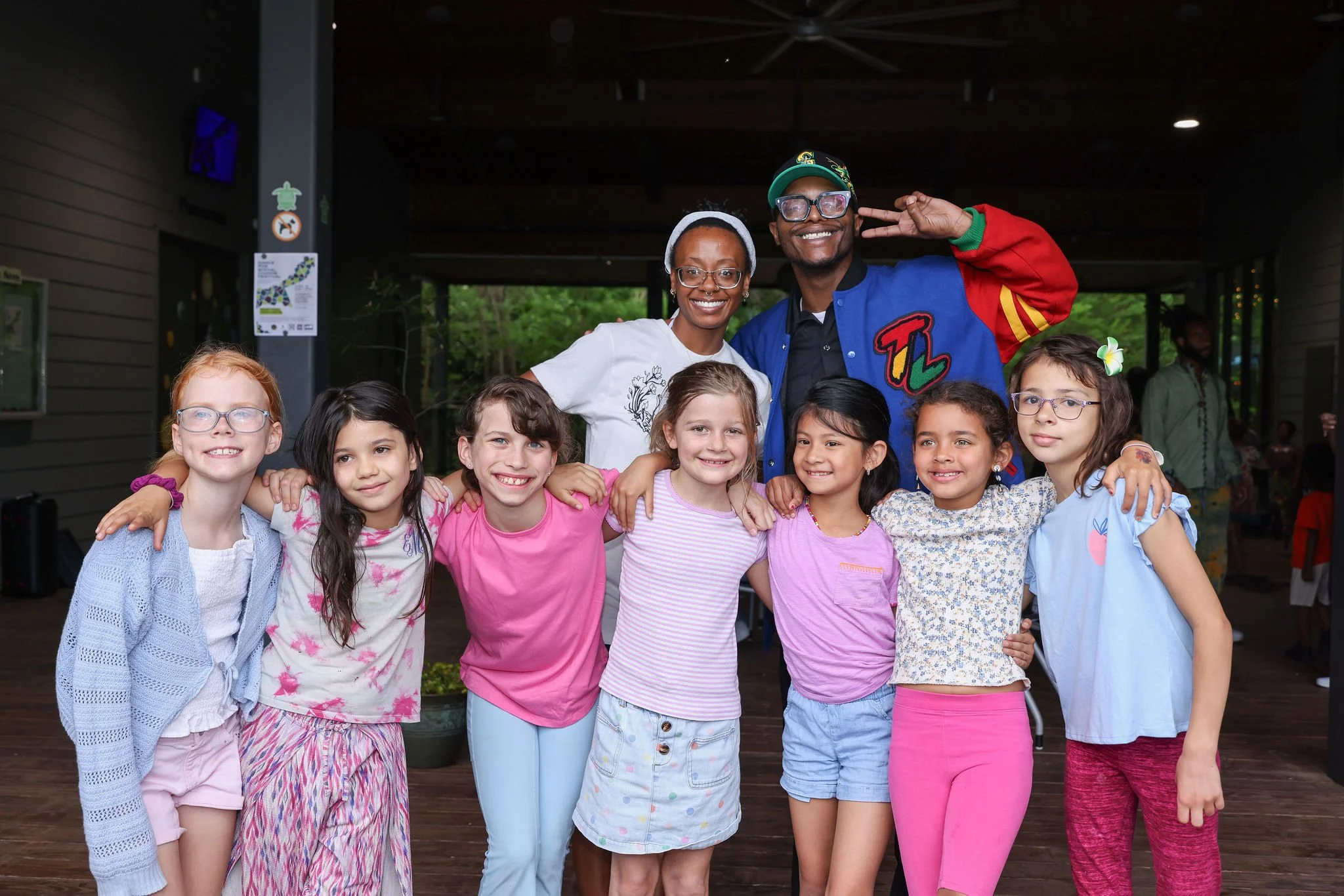 Group of children and two adults smiling for a photo indoors, with the adults standing behind the children.