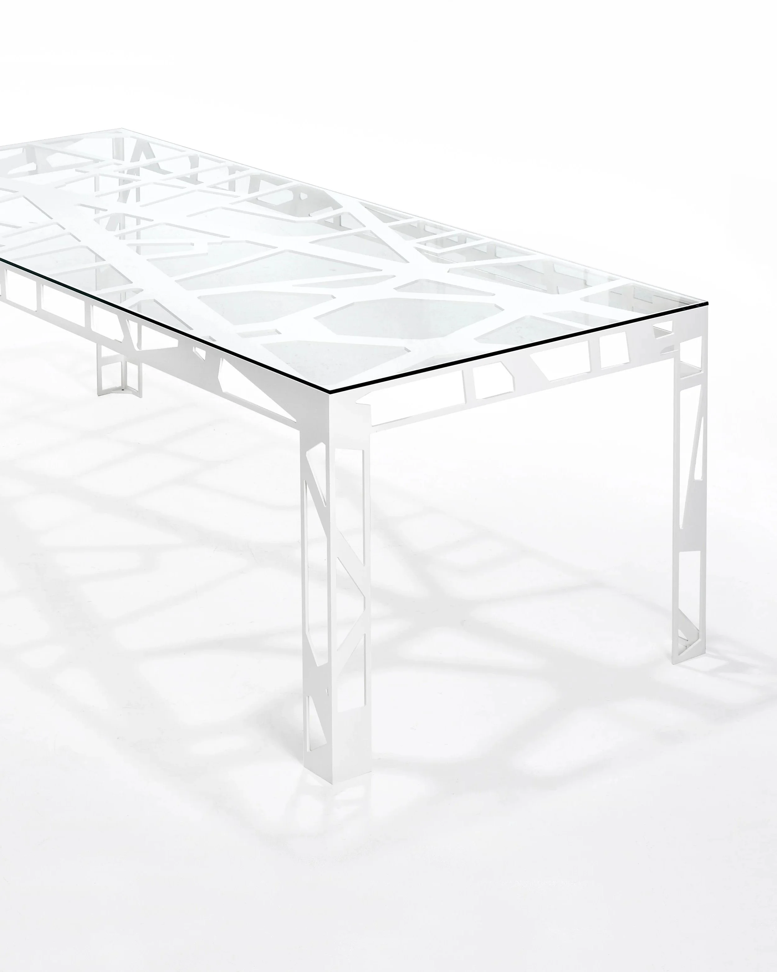 A modern white table with a glass top and geometric cutout design, set against a white background.
