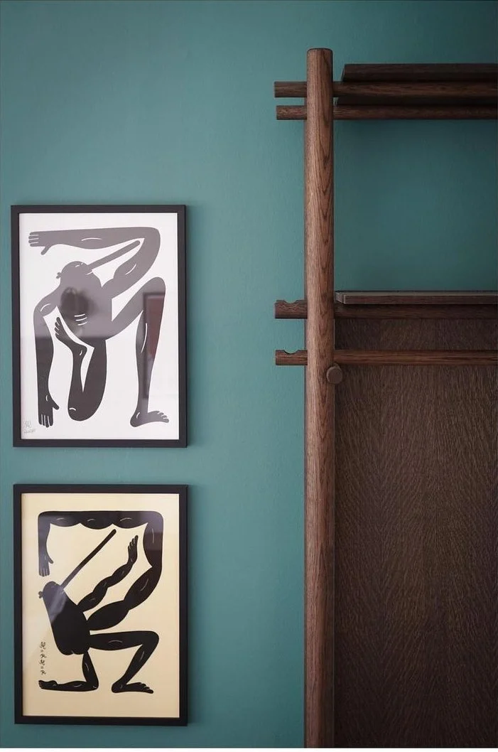 Two abstract art posters on a teal wall, one in black and white and the other in black and yellow, beside a wooden shelf.
