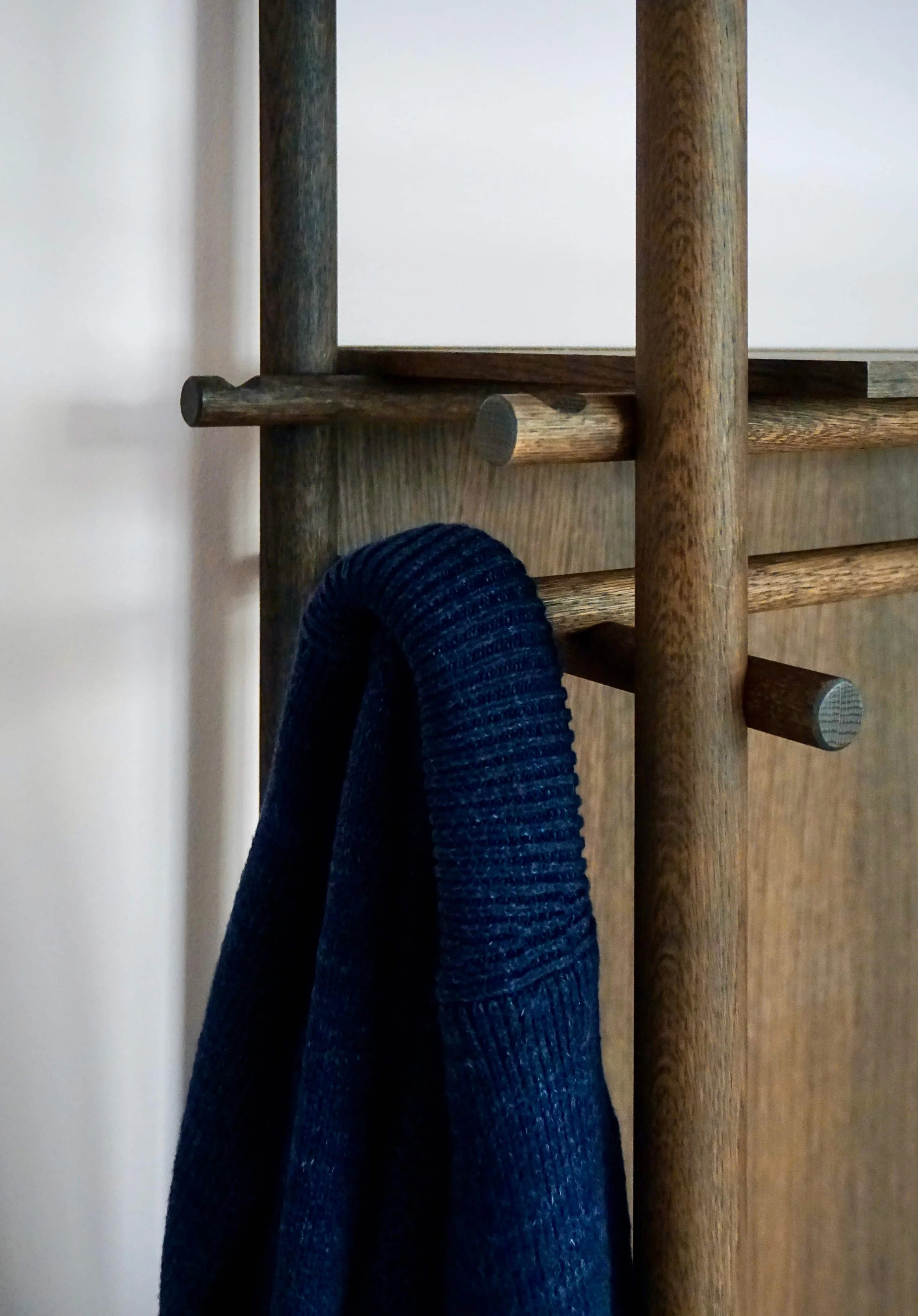 Close-up of wooden furniture with a dark-colored knitted fabric object hanging on it, against a white wall.