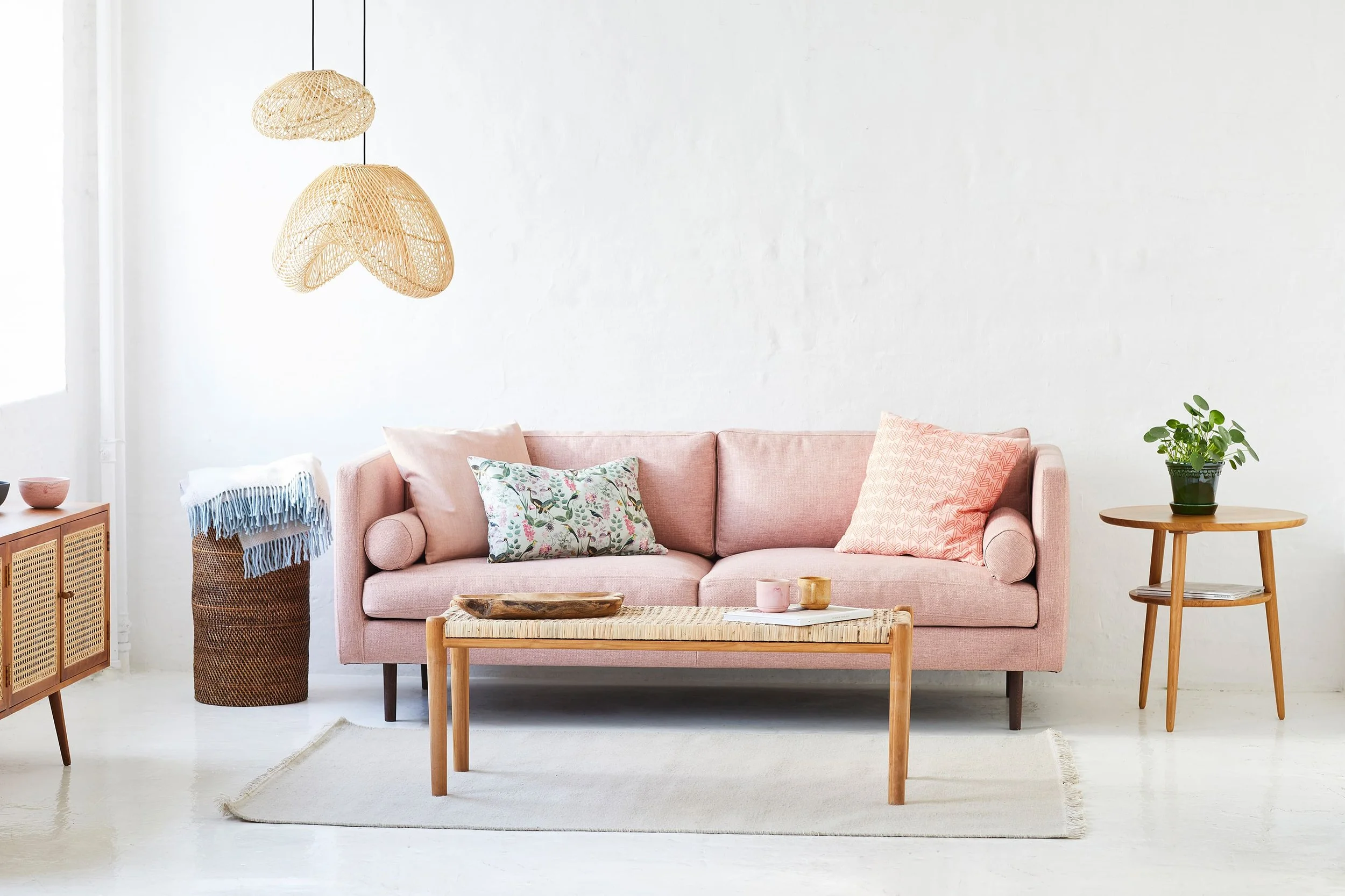 A pink sofa with multiple patterned and pastel-colored pillows, a wooden coffee table with decorative items. Sofa 01 by Mark de Vos Dalhoum architect and furniture designer